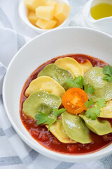 Close-up of a white bowl with ravioli served on tomato sauce bedding, vertical shot, selective focus