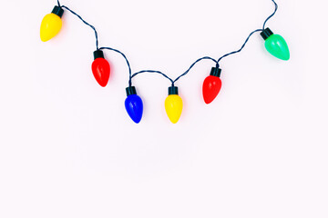 Colorful festive lights on white background. Red, blue, yellow and green bulbs hanging over white...