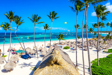 Beach vacation. Aerial drone view of tropical white sandy Bavaro beach in Punta Cana, Dominican Republic. Amazing landscape with palms, umbrellas and turquoise water of atlantic ocean - obrazy, fototapety, plakaty