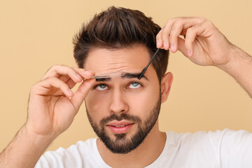 Young man correcting eyebrow shape on color background