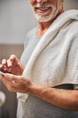 Gladsome senior citizen with a smartphone and a towel