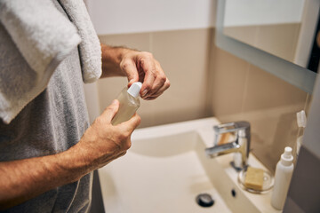 Man in the bathroom opening a bottle with a body-wash