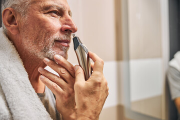 Smiley senior man grooming his nose hair with a trimmer