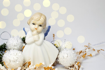 A statuette in the form of an angel stands among confetti on a light background with bokeh. Holiday...