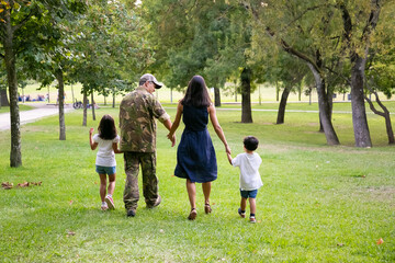 Military man and his family walking in park, kids and parents holding hands. Full length, back view. Family reunion or military father concept