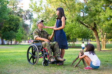 Fototapeta premium Little girl arranging firewood for campfire outdoors while her mom and disabled military dad holding hands and talking. Disabled veteran or family outdoors concept