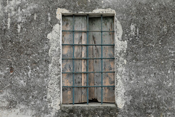cracked and dirty house facade with old window with wood and steel elements, the shutter is closed and space for text