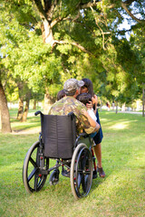 Disabled retired military father returning home, hugging and kissing wife and two kids. Back view....