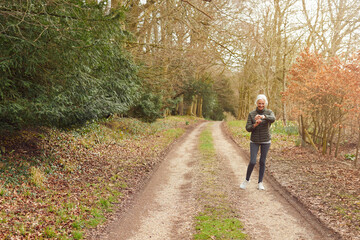Obraz premium Senior Woman Running In Autumn Countryside Exercising Checking Smart Watch Fitness Activity App