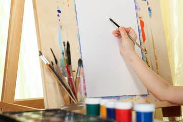 artist's hand holds paint brush on the background of the easel