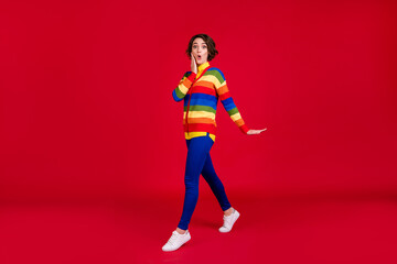Fototapeta na wymiar Full length profile photo of beautiful attractive lady walk down street amazed excited expression arm cheek wear rainbow jumper cardigan trousers shoes isolated bright red color background