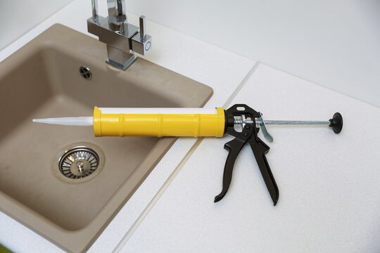 yellow sealant gun with sealant tube is on kitchen sink