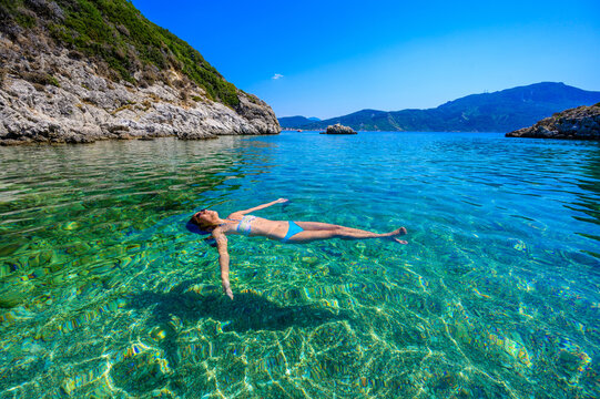 Girl with sun hat relaxing and swimming at Porto Timoni beach at Afionas is a paradise double beach with crystal clear azure water in Corfu, Ionian island, Greece, Europe