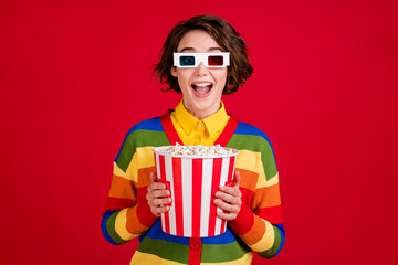 Photo of cheerful pretty lesbian lady hold hands big popcorn bucket watch movie cinema enjoy plot thrilling wear 3d spectacles striped cardigan jumper isolated bright red color background