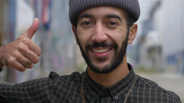 portrait of a handsome young muslim man smiling, showing a thumbs up in the street, close up portrait