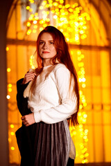 red-haired girl in the winter evening on the street against the background of Christmas lights