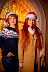red-haired girl with her mother in the winter evening on the street against the background of Christmas lights