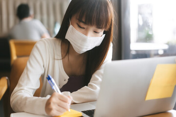 Young adult asian student female with face mask for virus corona or covid 19 study at cafe.