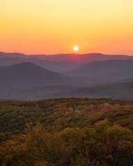 Warm golden sunlight shining across layers of rolling mountains during sunset. Overlook Mountain, New York. 