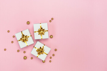 White gift boxes with golden bows and golden decorations on pastel pink background. Minimal styled holiday card. Flat lay, top view, copy space. 