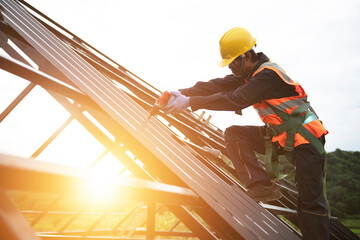 Asian construction workers wear safety straps while working on the roof structure of the building at a construction site. Roofer, using a pneumatic nail gun, install roof tiles. - obrazy, fototapety, plakaty