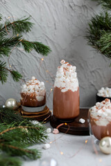 Three glasses of cocoa drink with ice cream and marshmallows. New Years hot drinks on a gray table with Christmas decorations.