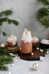Three glasses of cocoa drink with ice cream and marshmallows. New Years hot drinks on a gray table with Christmas decorations.