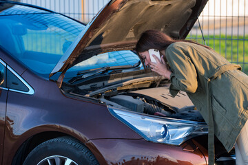 Young woman standing near broken car and calling for help or assistance. Calling to car mechanic for auto repair.