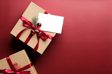 Carton gift box decorated red ribbon bow and blank paper card mockup on marsala red background....