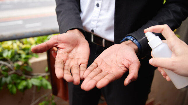 Close Up Of Businessman Having Hands Sprayed With Sanitiser During Health Pandemic