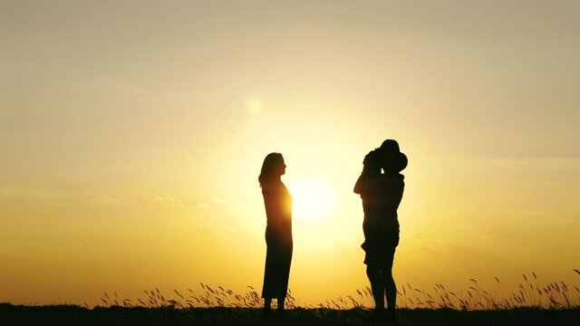 Silhouette of a happy family against a bright sunset. Father and mother kiss and hug their son.