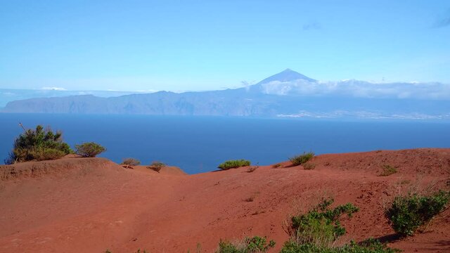 La Gomera - Rote Wüstenlandschaft mit einigen Büschen im Norden oberhalb von Agulo mit Blick nach Teneriffa mit Teide