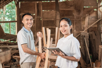 young entrepreneurs stand holding a tablet pc and workers standing behind while at the workshop