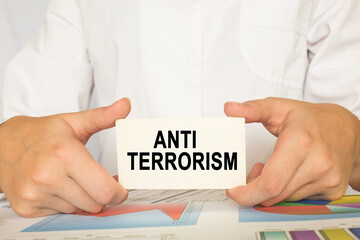 a man in the office holds a card with text ANTI TERRORISM. business concept