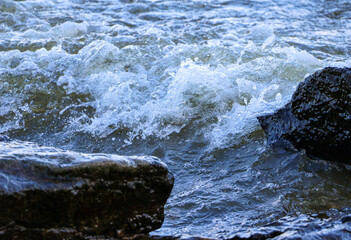 waves run onto the shore and crash against the rocks, creating many splashes and splashes near the shore. river surf in stormy weather near a stone pebble coast with foamy splashing waves.