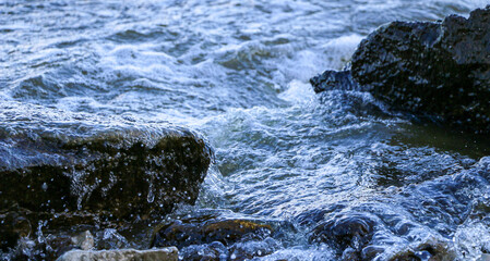 waves run onto the shore and crash against the rocks, creating many splashes and splashes near the shore. river surf in stormy weather near a stone pebble coast with foamy splashing waves.