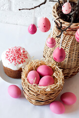 Fototapeta na wymiar Easter composition with decorated tree branches in a wicker vase, pink colored eggs in wicker basket and Easter cake