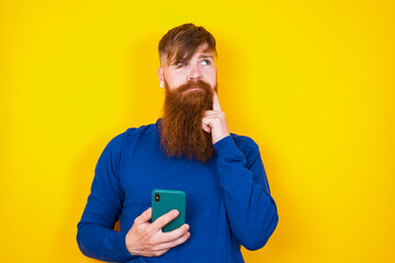 Image of a thinking dreaming Young handsome red haired bearded man standing against yellow wall...