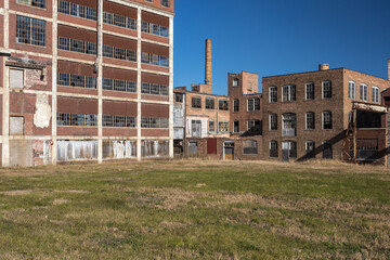 Obraz premium Open field in front of abandoned factory buildings with clear blue sky
