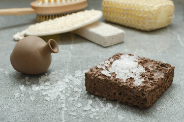Closeup of clay bottle of aroma oil, stone and sea salt for scrubing, sponges on the grey surface