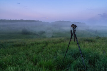 Modern professional camera on a tripod, outdoor shooting in the wild. The camera on a tripod shoots a foggy landscape.