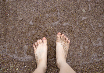 Closeup feet of young woman standing on sea shore;  sea wave reaching the feet. Summer activity. Beautiful holiday background