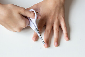 
Child cuts his fingernails with scissors on a white background. Close-up.
