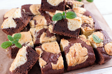Trend baking Brookies chocolate brownies and cookies homemade cake sliced by squares with mint on parchment paper on a wooden table.