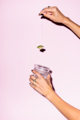 cropped view of woman holding lime above glass with alcohol drink on pink - obrazy, fototapety, plakaty