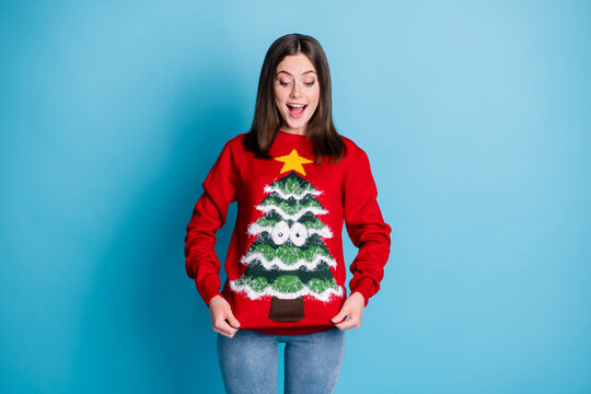 Photo Portrait Of Surprised Girl Pulling Ugly Christmas Sweater With Hands Smiling Looking Down Isolated On Pastel Light Blue Colored Background