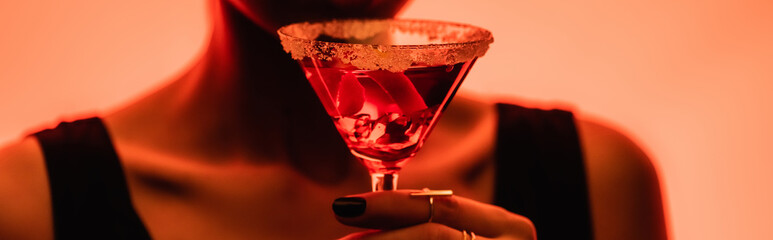 margarita cocktail with ice cubes and salt in hand of woman on blurred orange background, banner