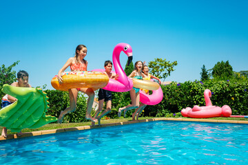 Group of children with inflatable toys donut run and jump in the water pool smiling happily...