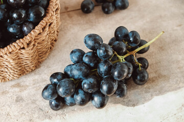 Bunch of black grapes in a round wicker basket on a old wooden table. Copy, empty space for text