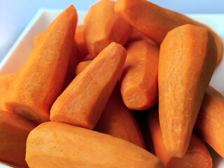 A white plate of peeled carrots stands on a white background. 